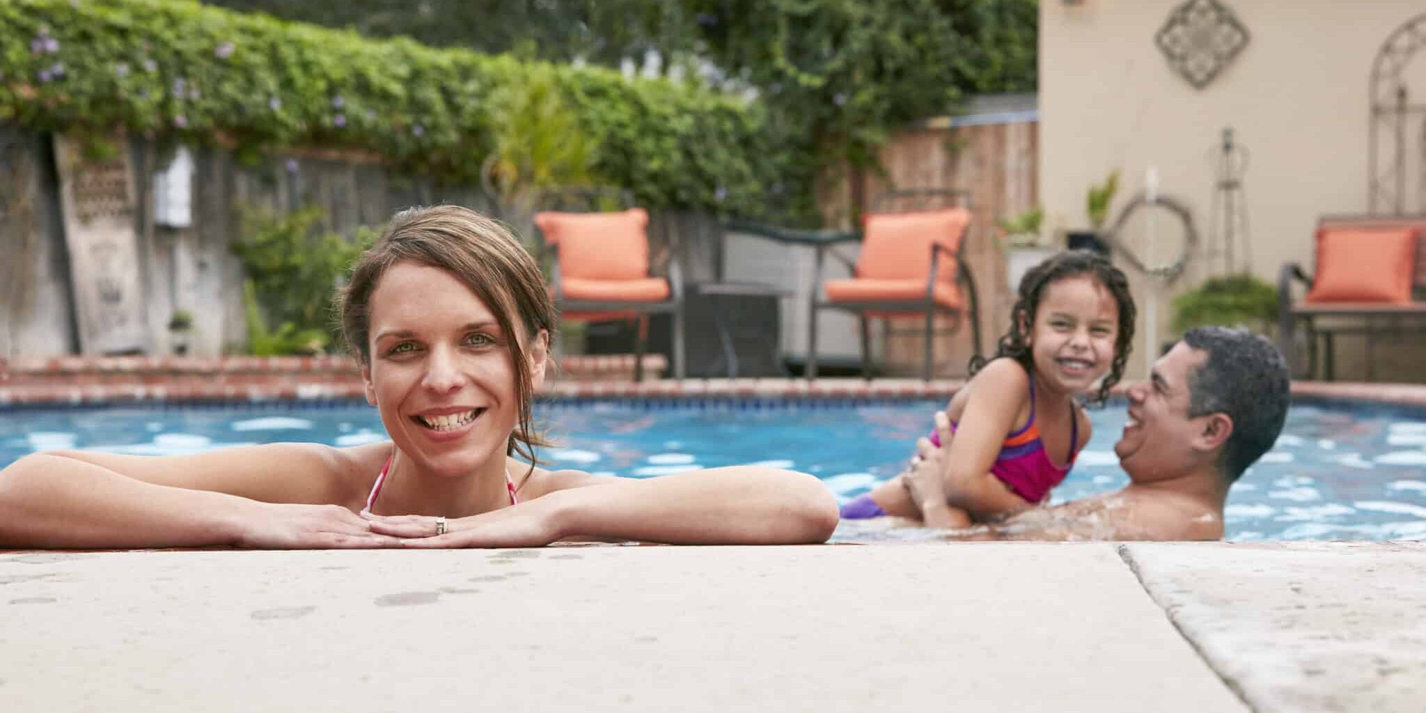 Head and shoulders of mid adult woman with family in pool looking at camera smiling Head and shoulders of mid adult woman with family in pool looking at camera smiling