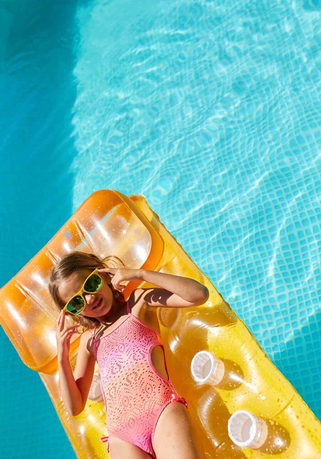 Little girl in sunglasses relaxing in swimming pool, enjoying suntans, swims on inflatable yellow mattress and has fun in water on family vacation, tropical holiday resort, view from above, copy space.
