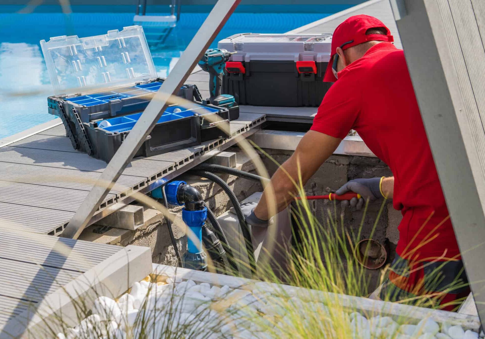 Closeup of Caucasian Professional Worker in Red Uniform Fixing Outdoor Swimming Pool Heating System Using Different Tools. Side View.